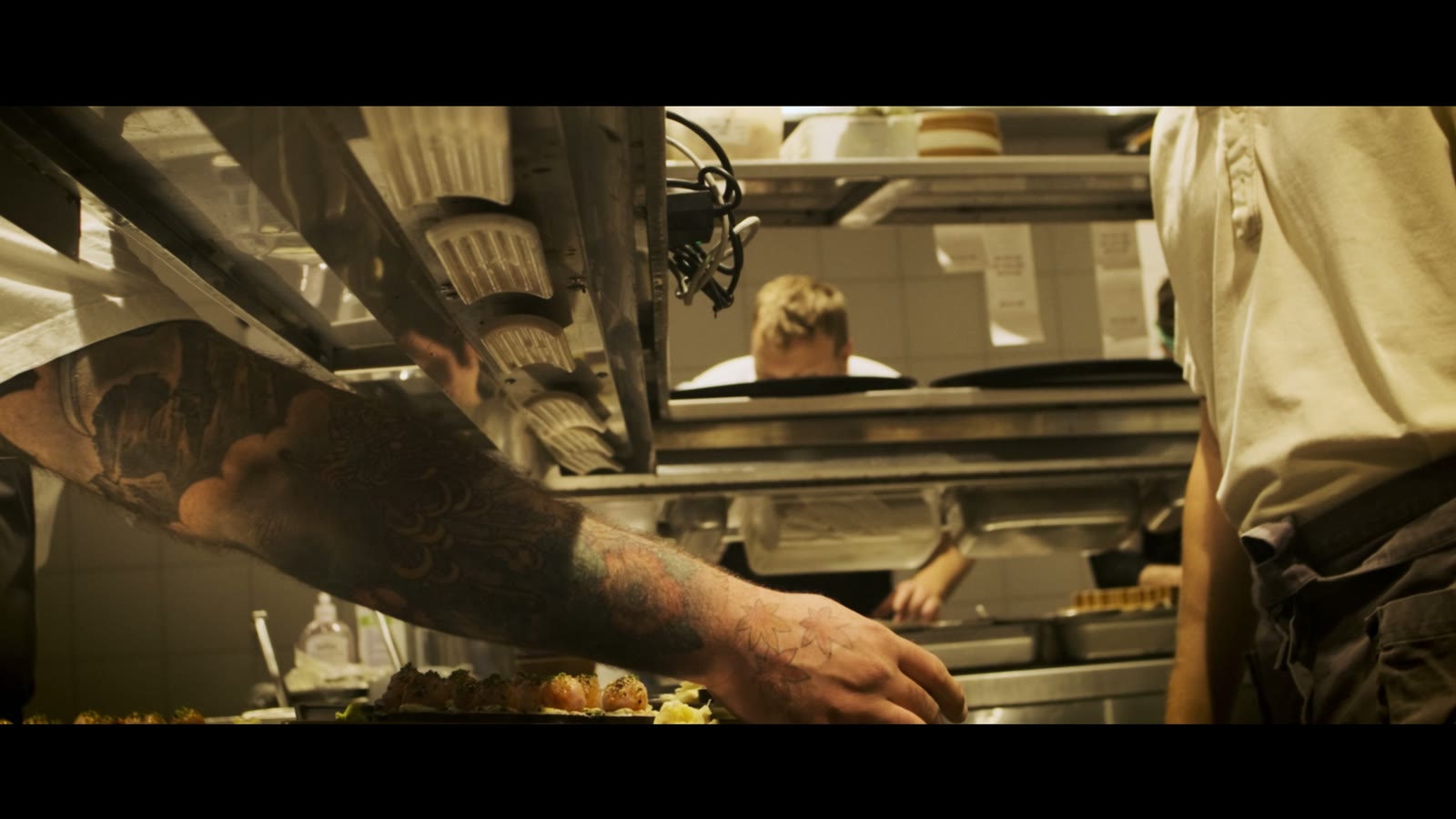 Tattooed forearm reaching across a warm-lit restaurant pass